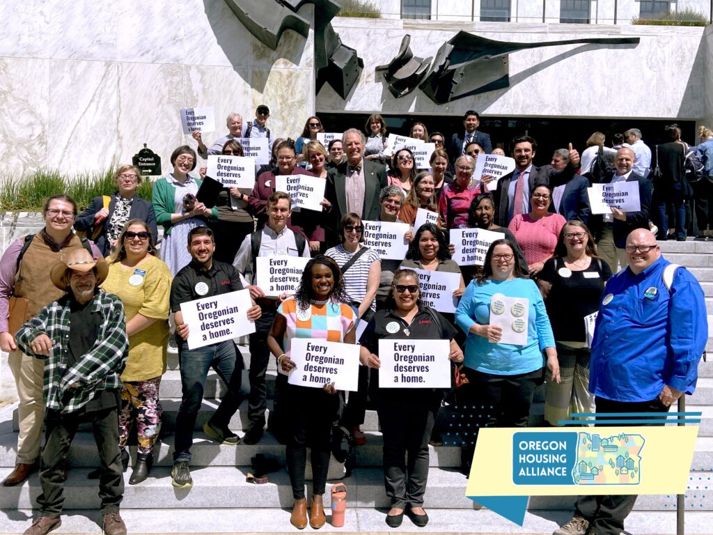 large group of people holding "every oregonian deserves a home" signs standing on the steps of the Oregon Capitol