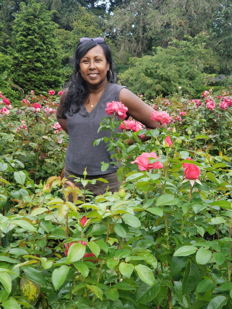 a picture of Roberta standing in a rose garden with trees in the background