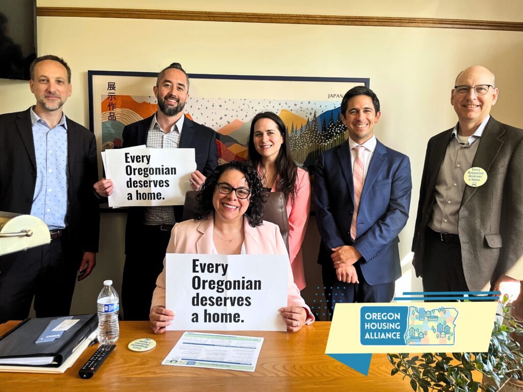group of people posing together smiling, two of them holding "every oregonian deserves a home" signs.