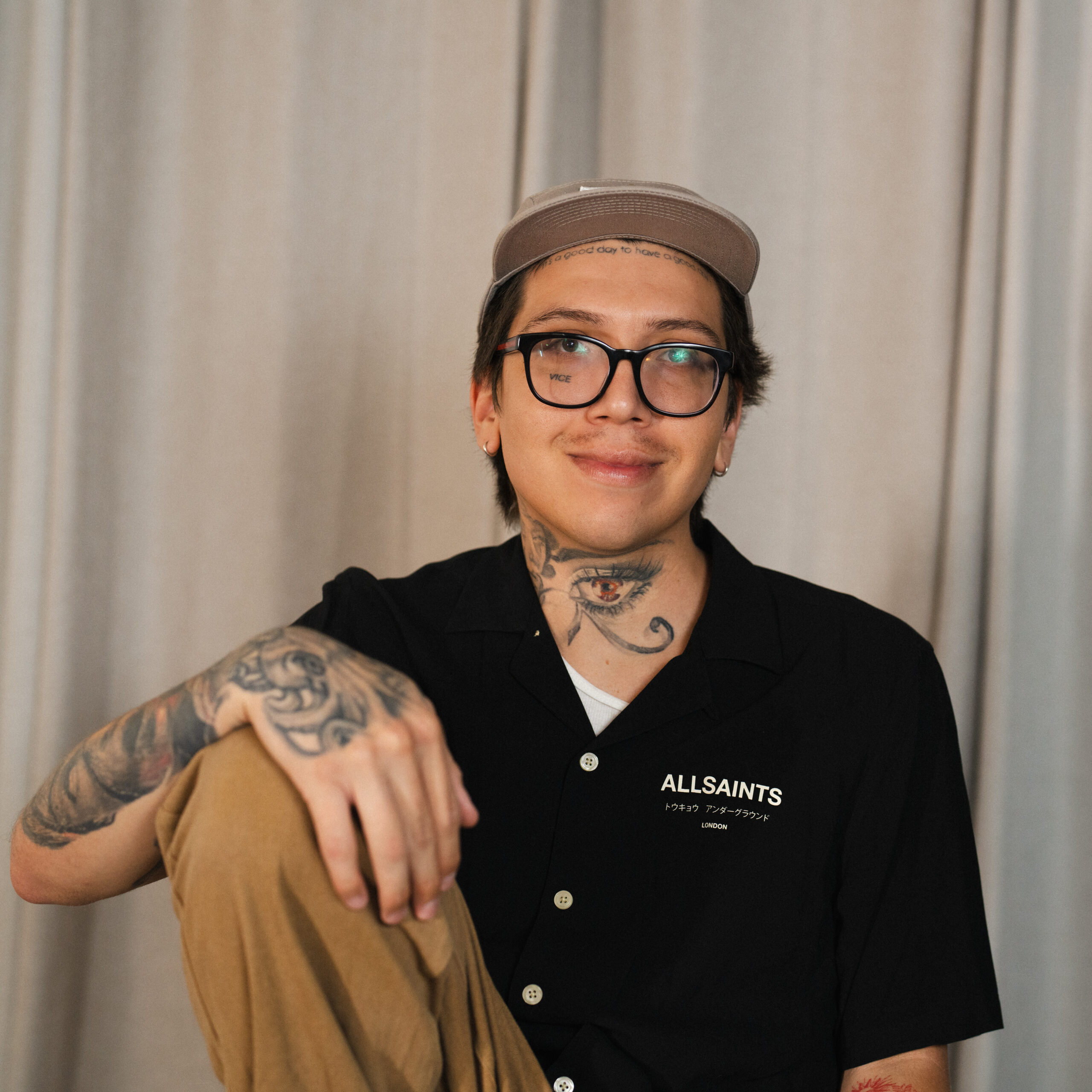 image of man resting his hand on his knee, wearing a shirt that reads "AllSaints".